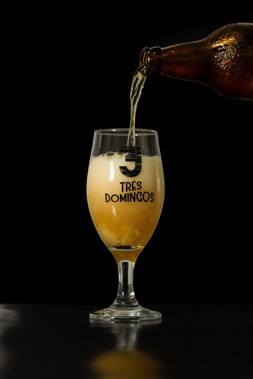 Cerveja Três Domingos sendo servida em taça com espuma cremosa